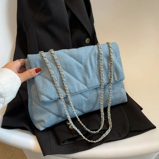 Blue Shoulder Bag in the color baby blue held in hand on a black jacket and on a white desk