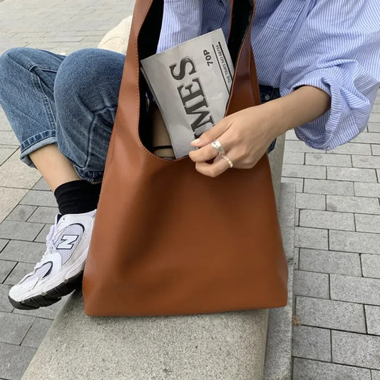 Brown Tote Bag Leather filled with a newspaper and worn by a woman sitting on a stone bench